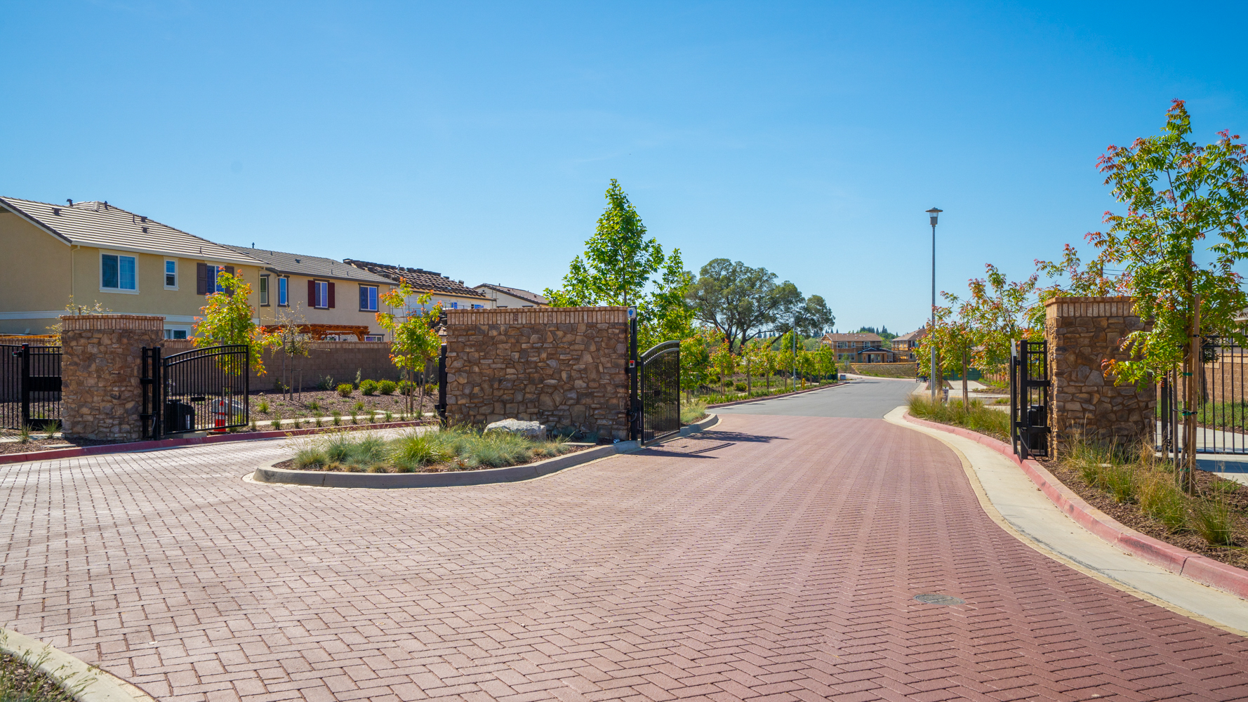 A brick road with a fence and trees on the side.
