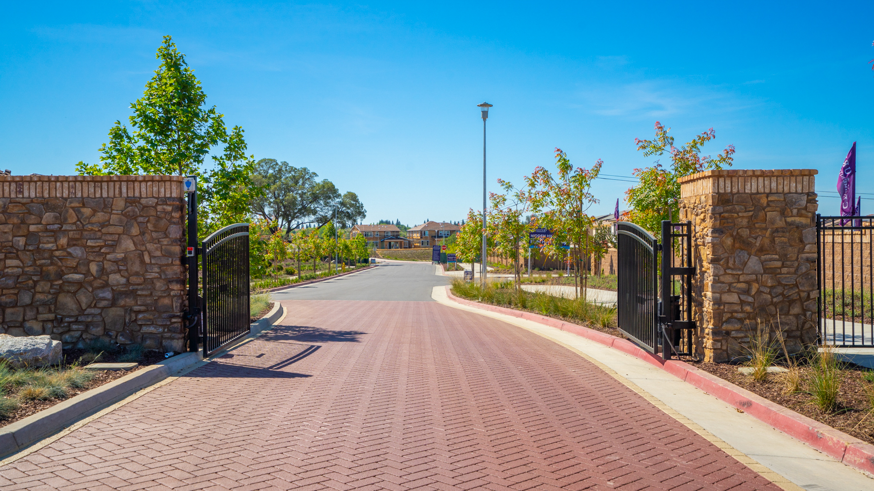 A brick road with a fence and trees on the side.