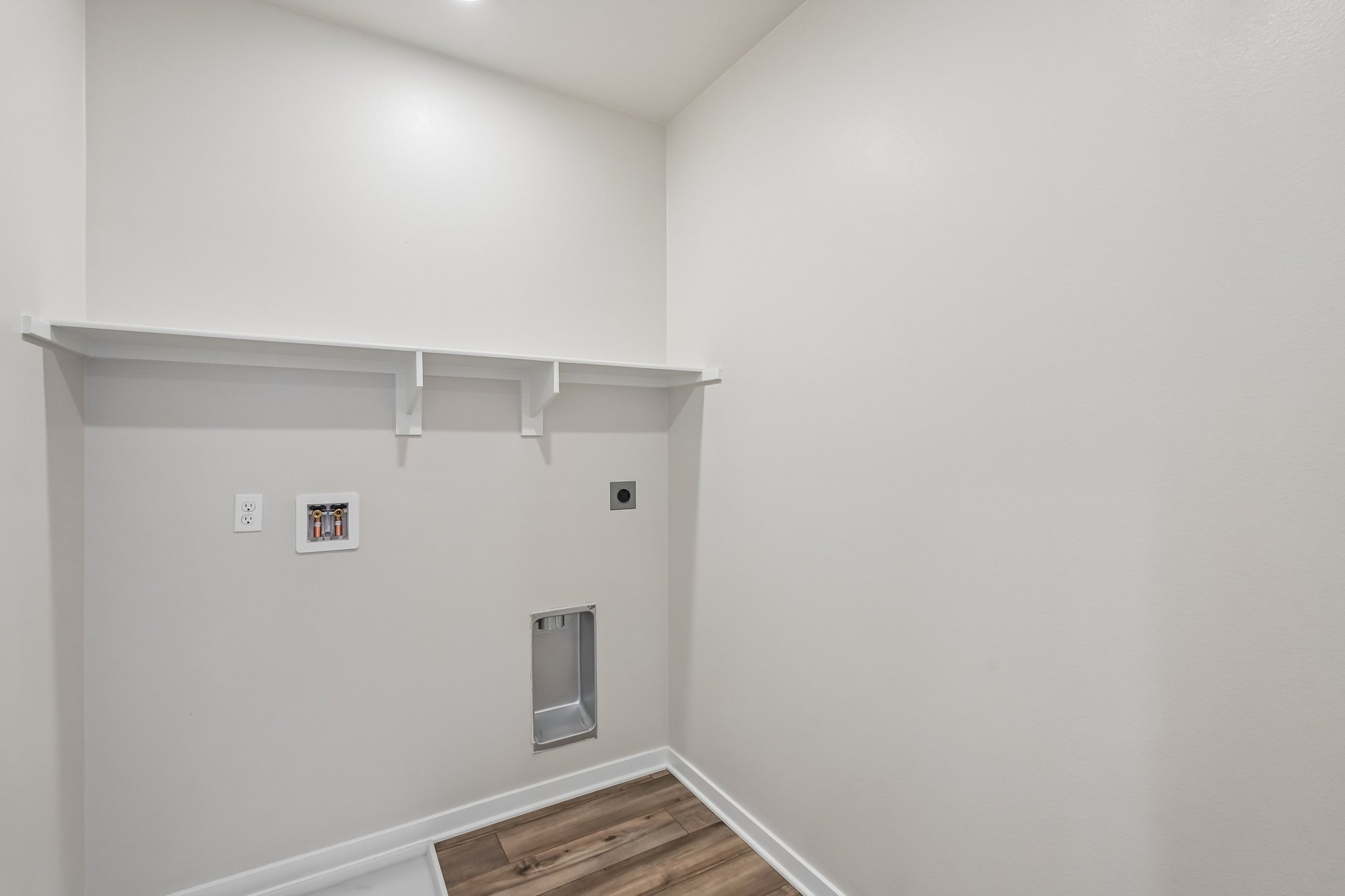A white wall with a shelf and a wood floor.
