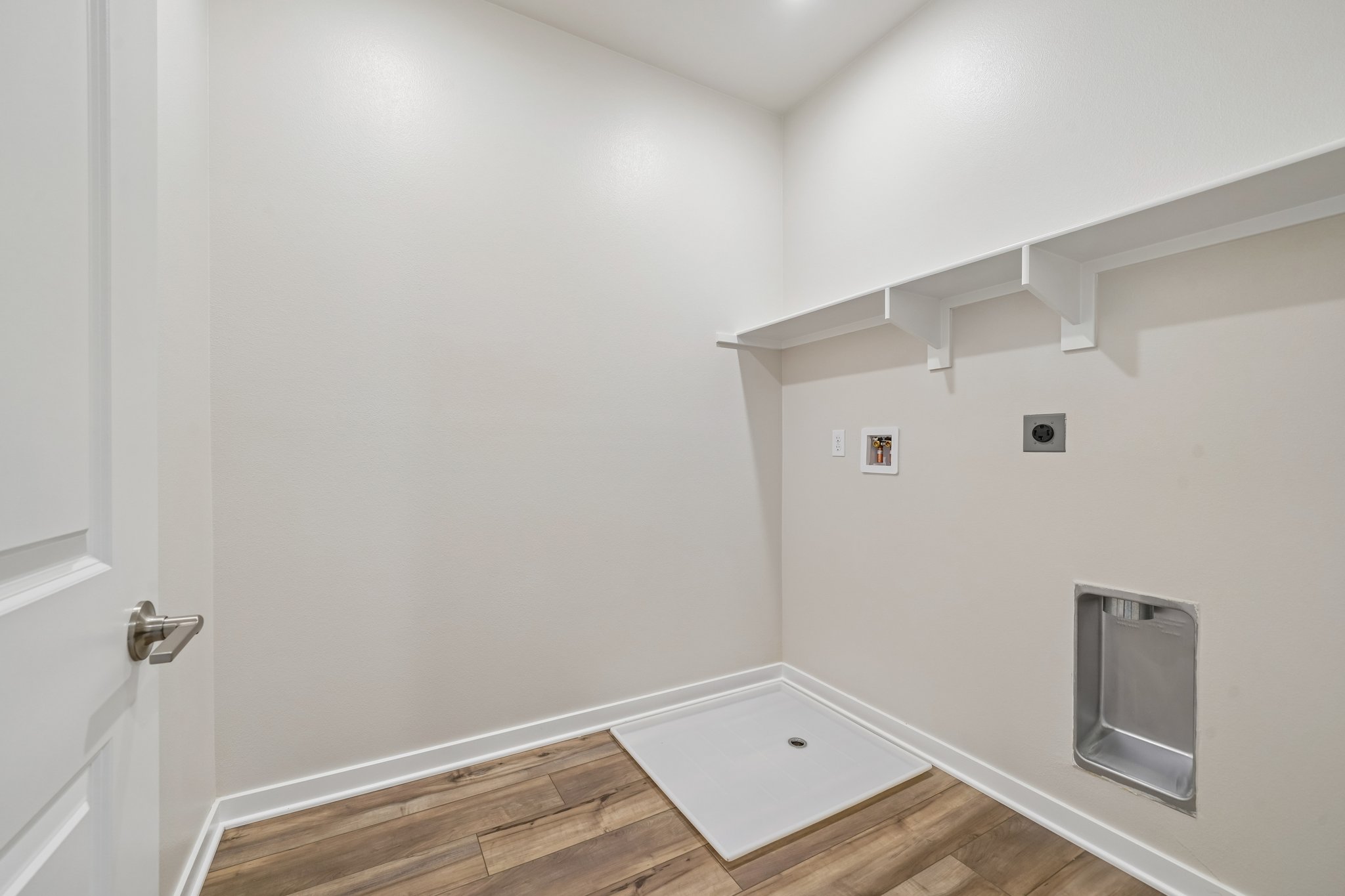 A room with a wood floor and a white wall with a light on it.
