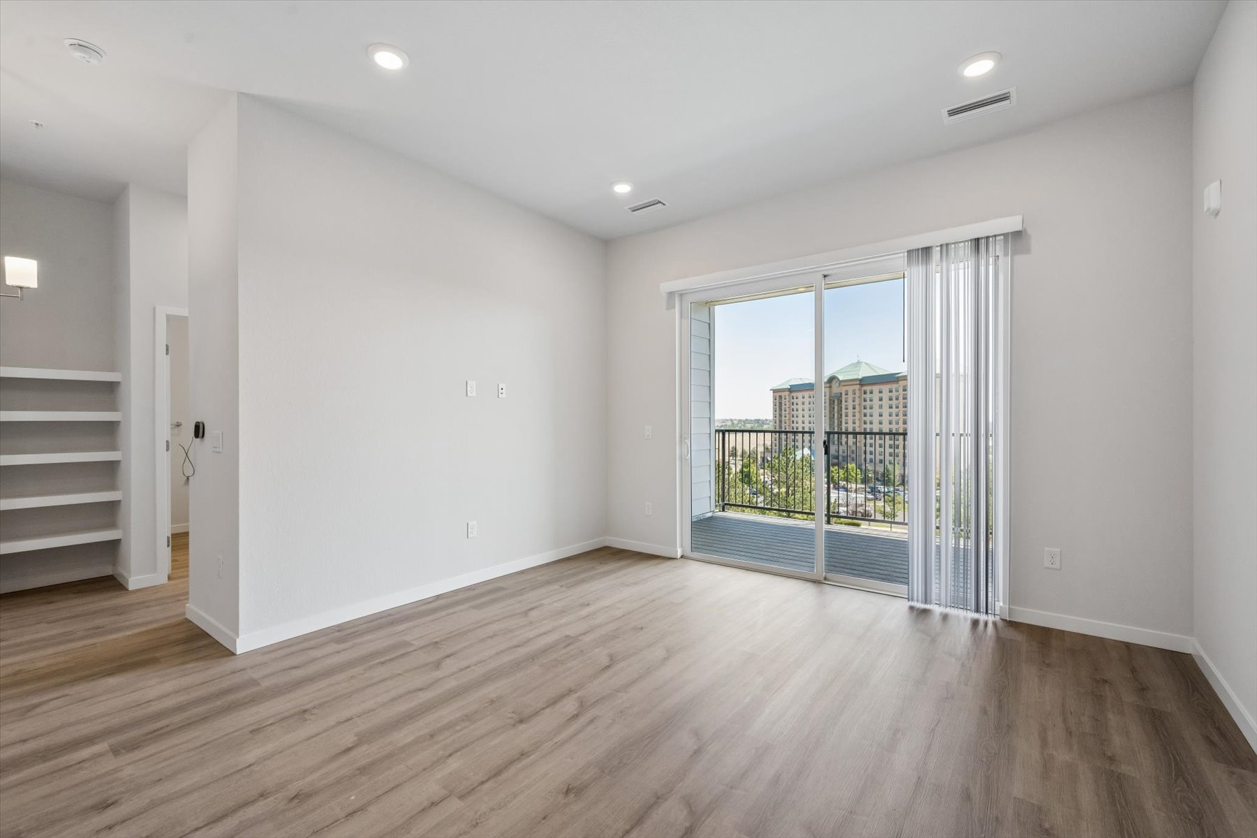 A room with a wood floor and a glass door leading to a balcony.