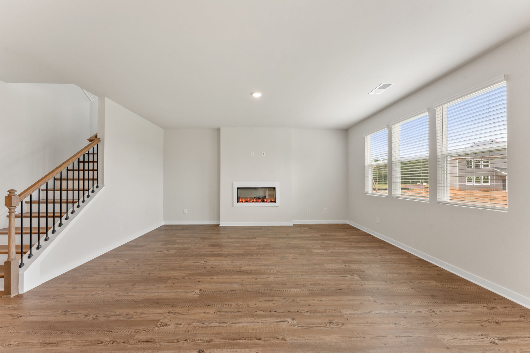 A large empty room with a wood floor and a staircase.