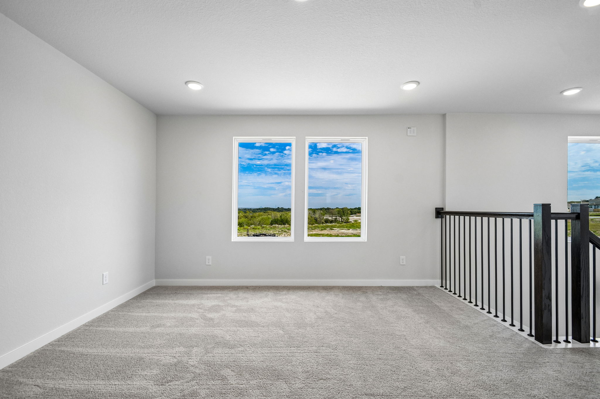 A room with a black railing and a window with a view of a tree outside.