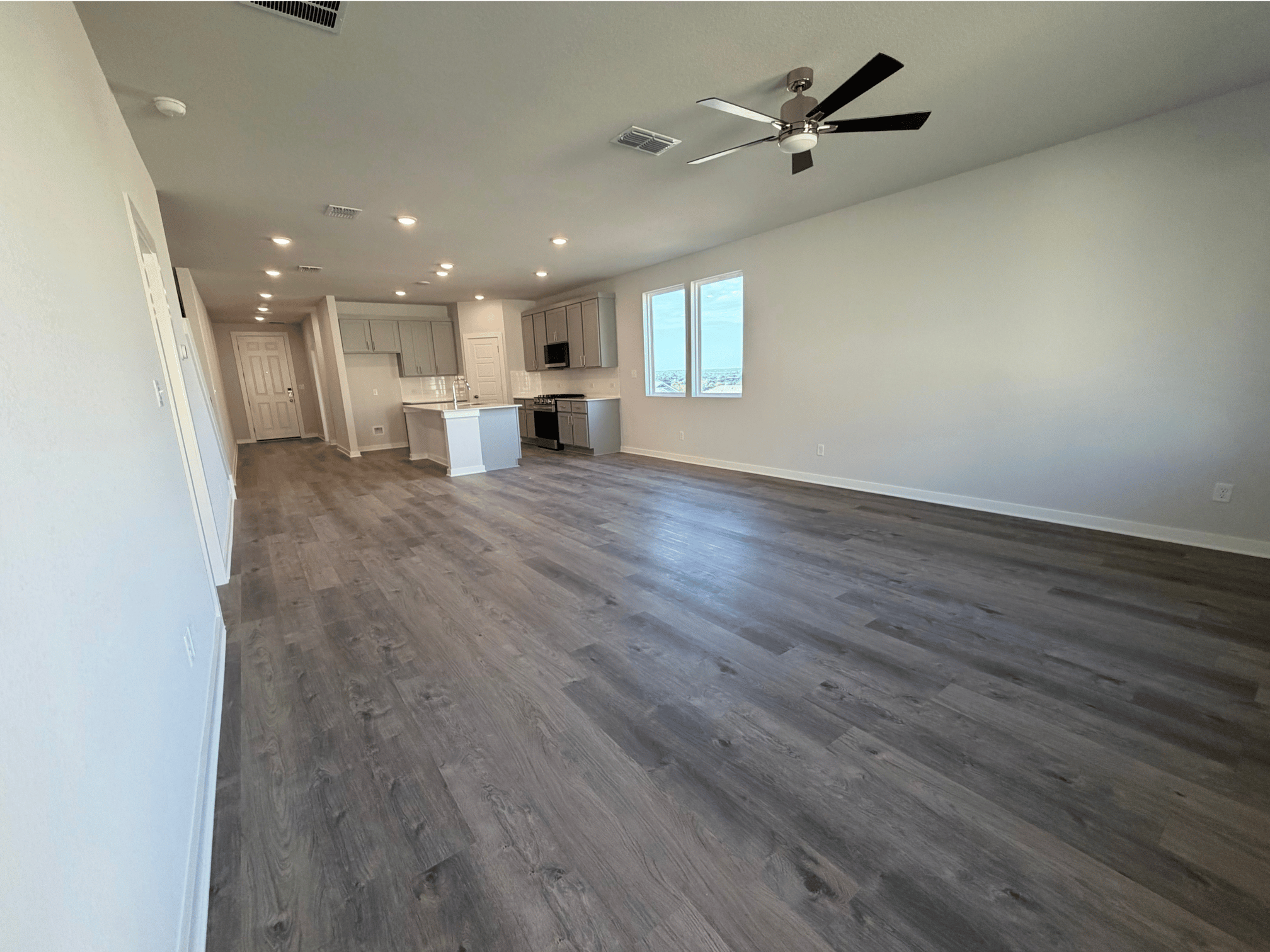 A large empty room with a wood floor and a ceiling fan.
