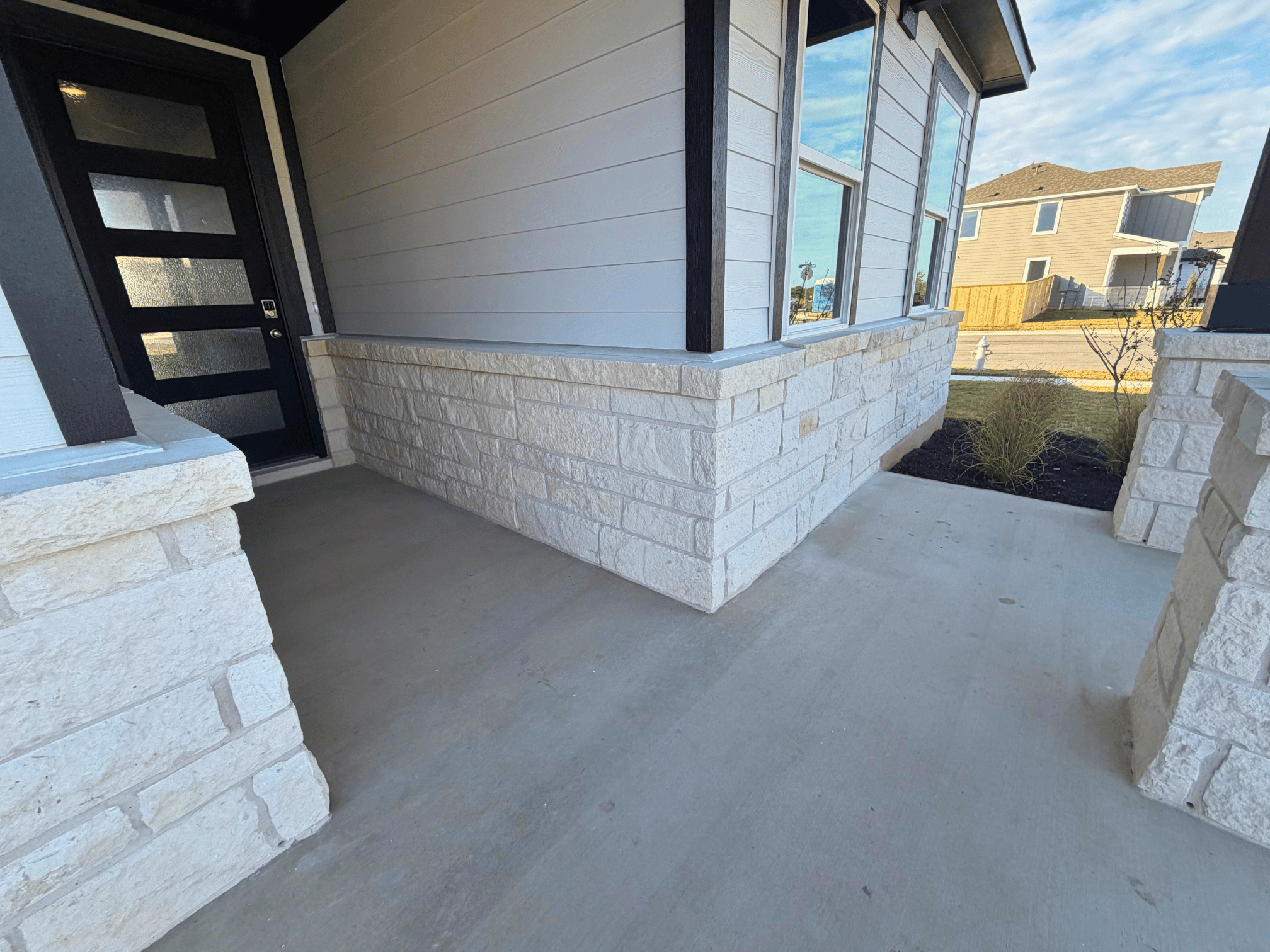A concrete patio with a door and a stone wall and a building.