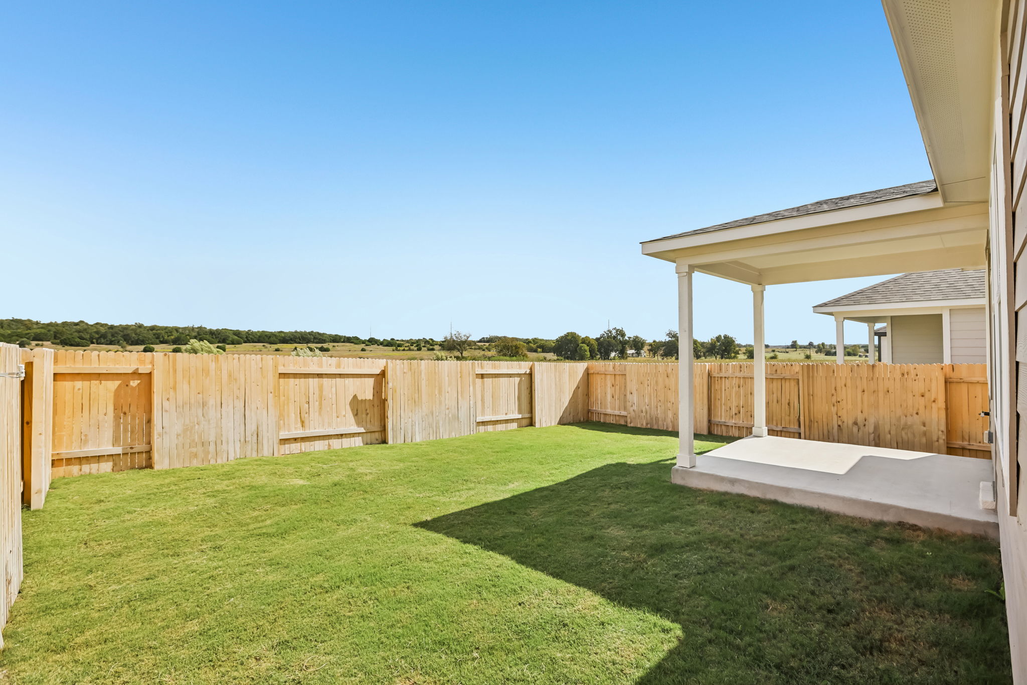 A fenced in yard with a house and a grass field.