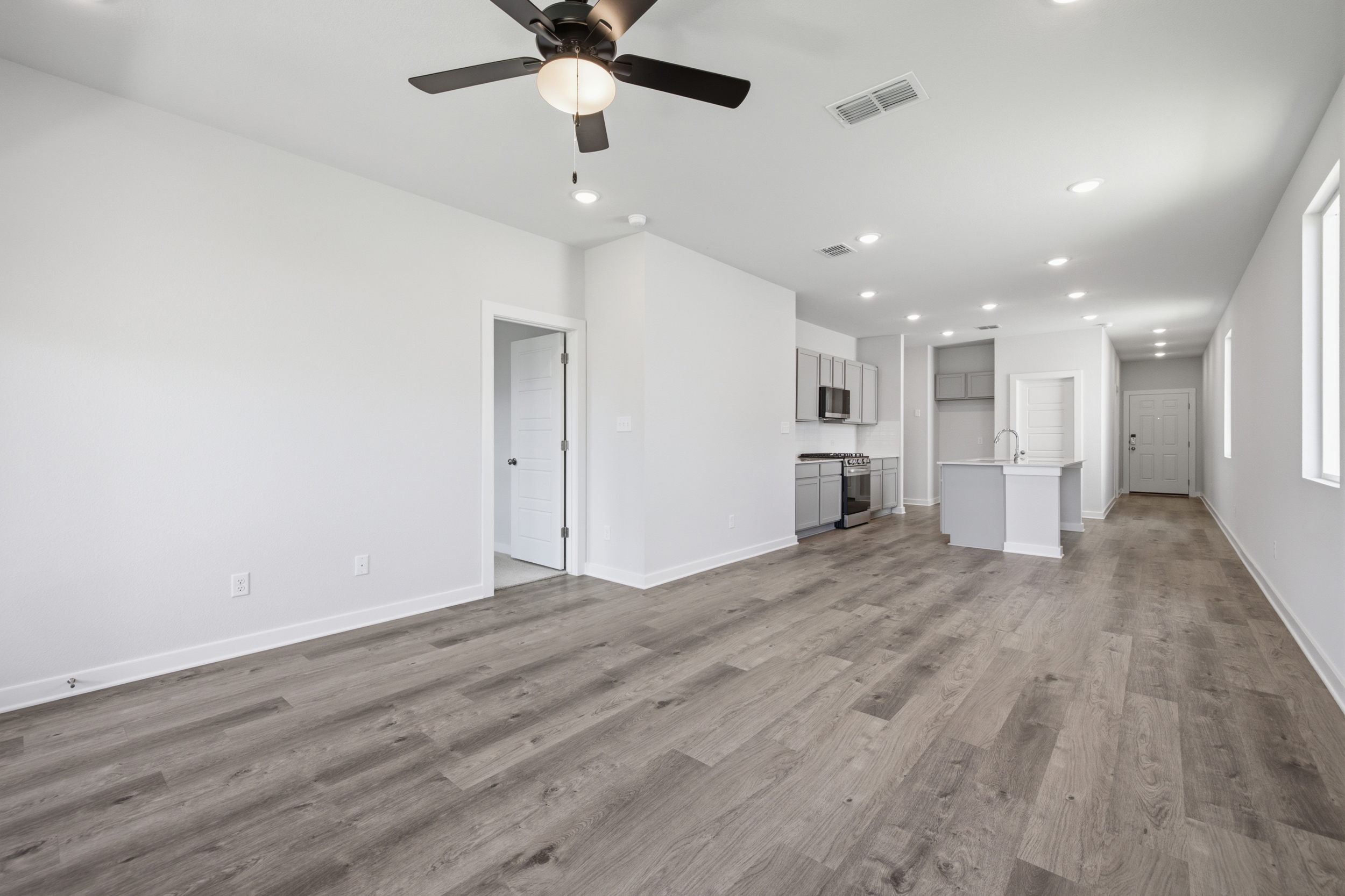 A large empty room with a ceiling fan and a wood floor.