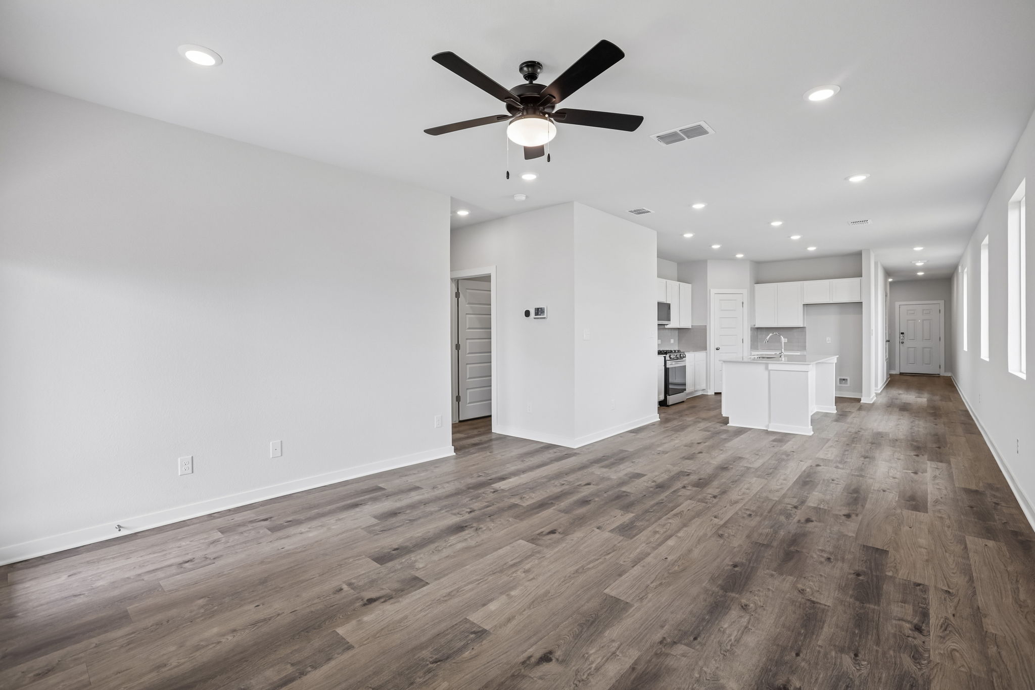 A large empty room with a ceiling fan and wood floors.