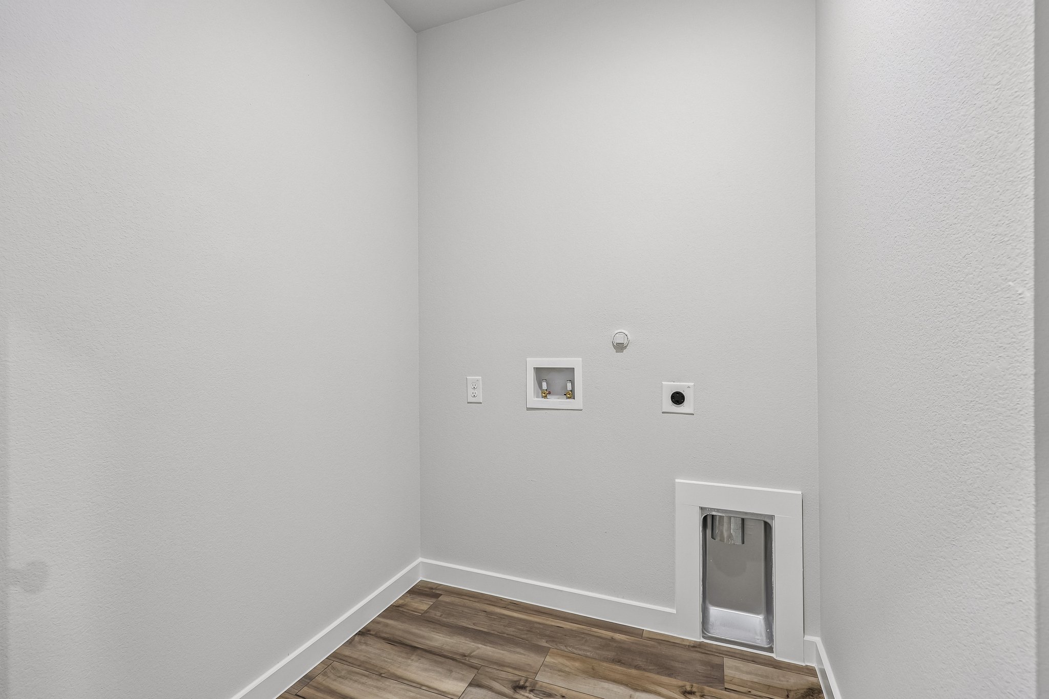 A room with a wood floor and a white wall with a light on it.