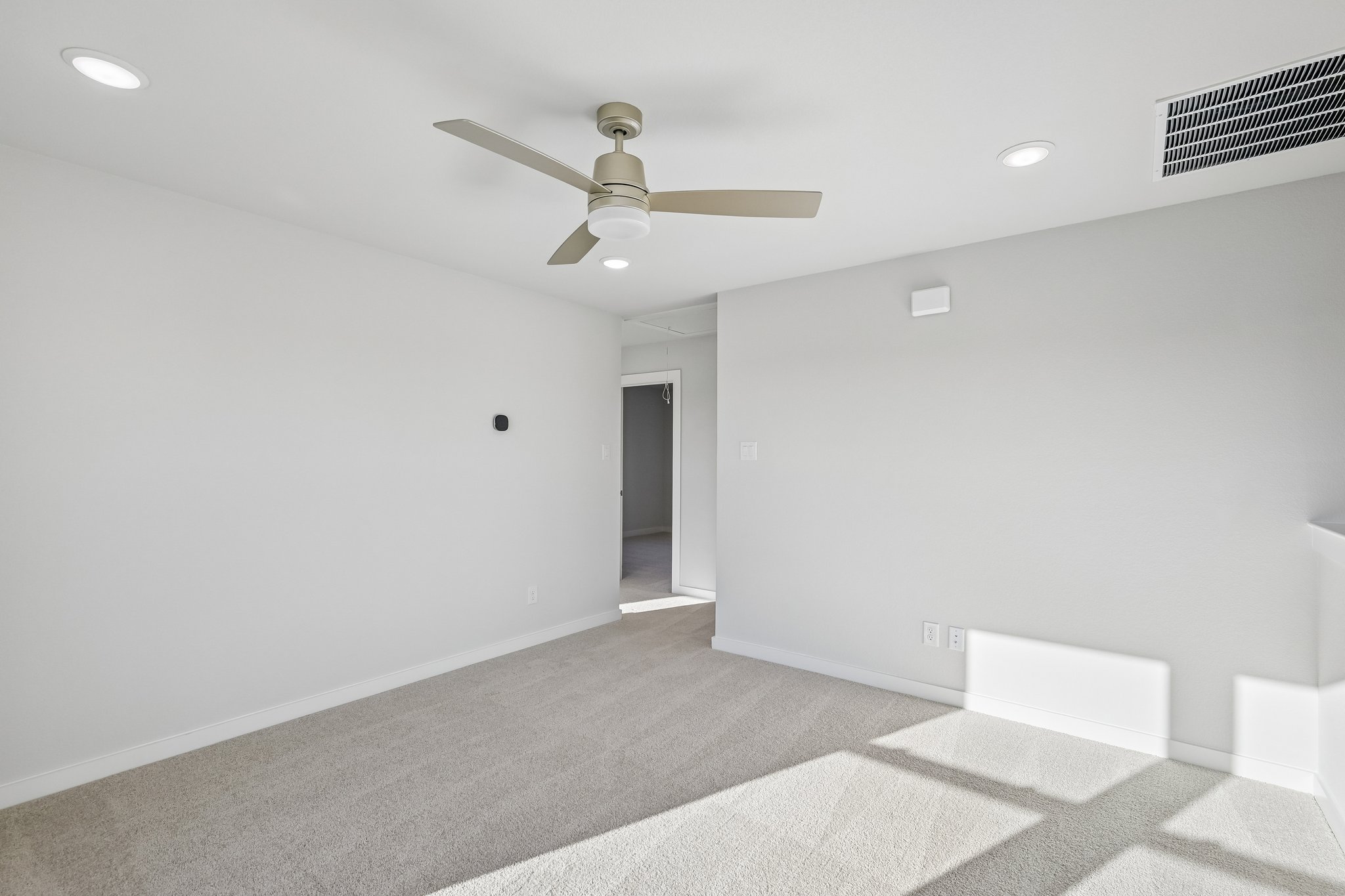 A room with a ceiling fan and a carpet.