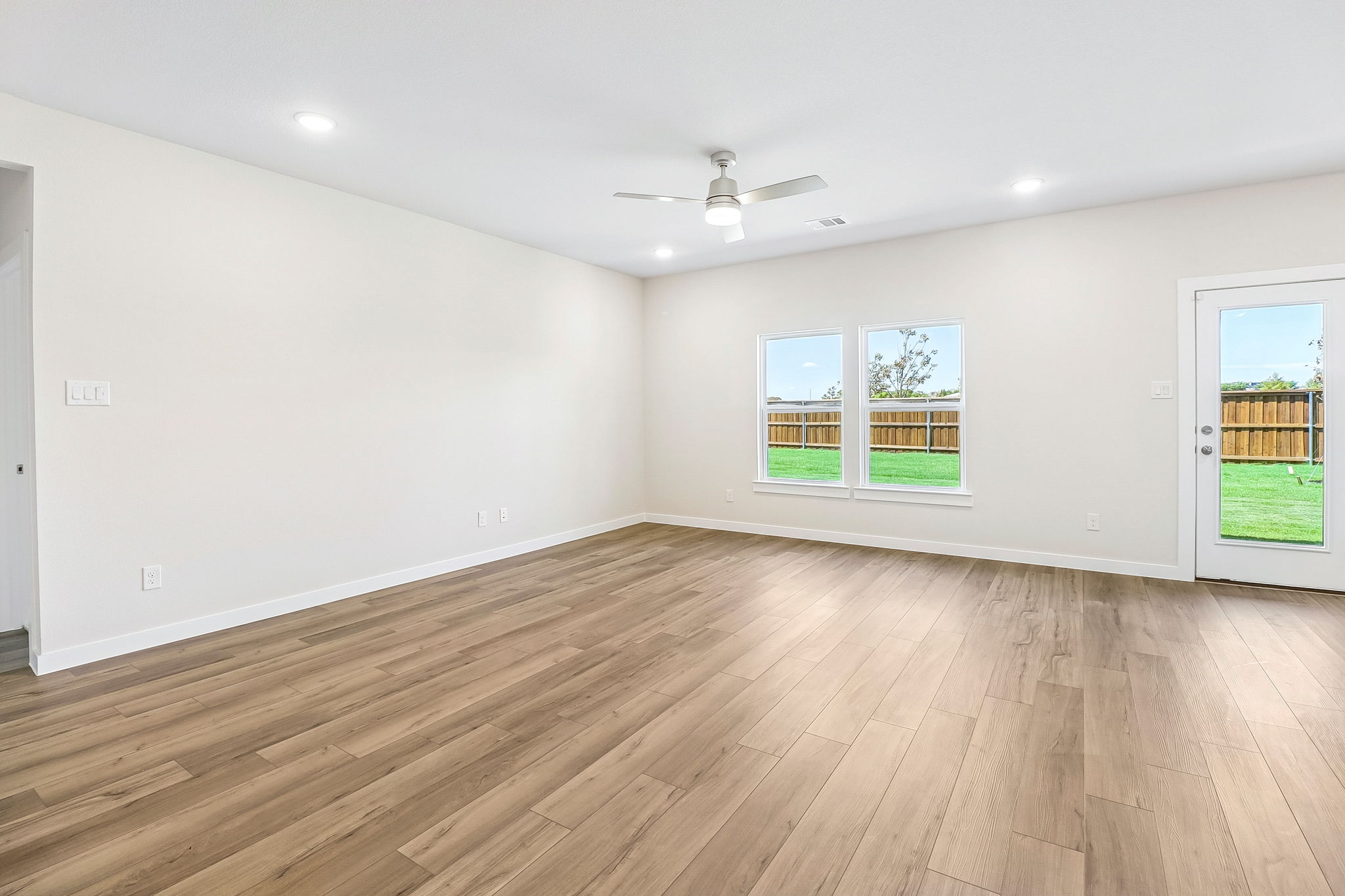 A room with a wood floor and a ceiling fan and windows.