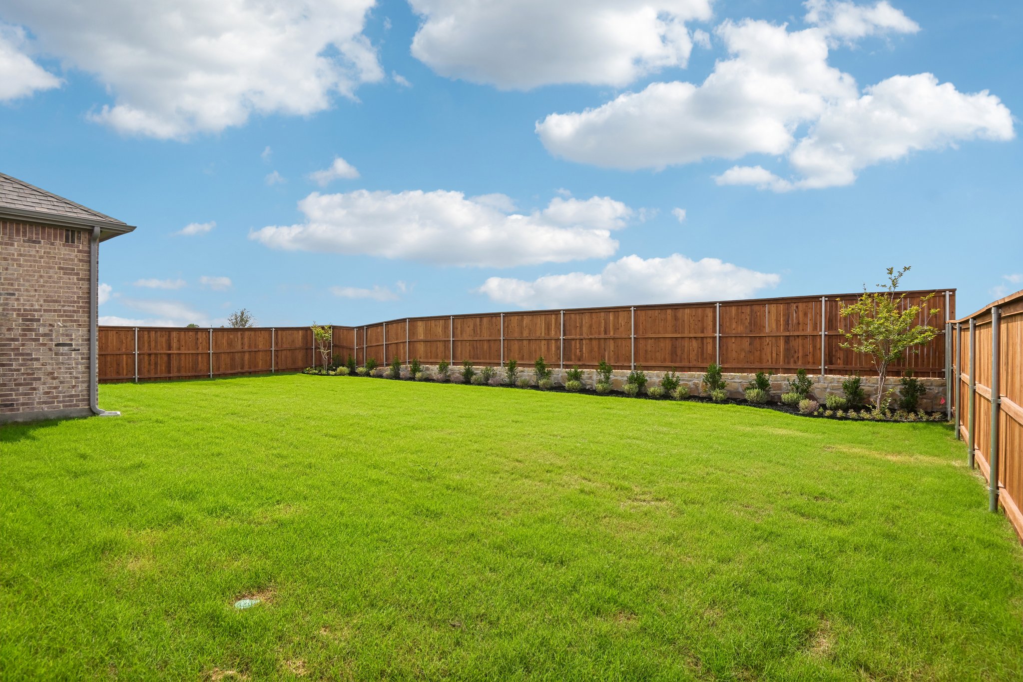 A fenced in yard with a brick building and trees.