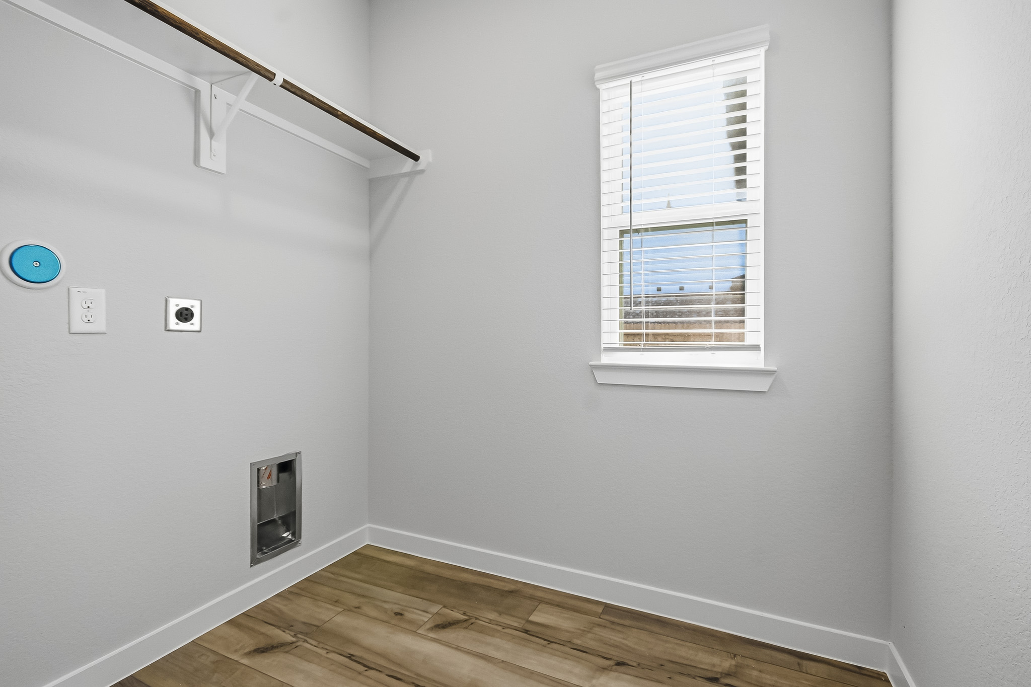 A room with a wood floor and a window with a vent.