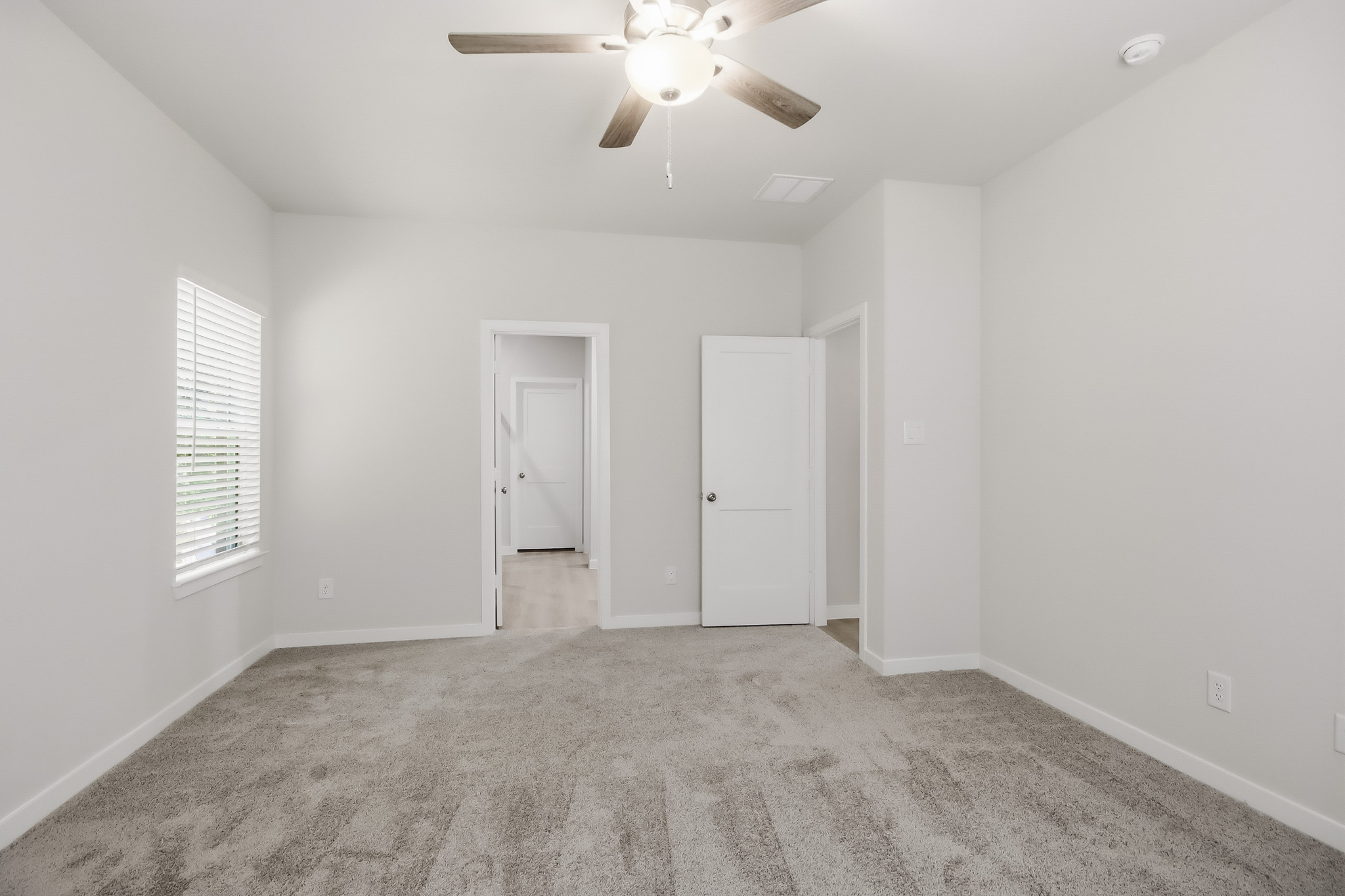 A room with a ceiling fan and white walls.