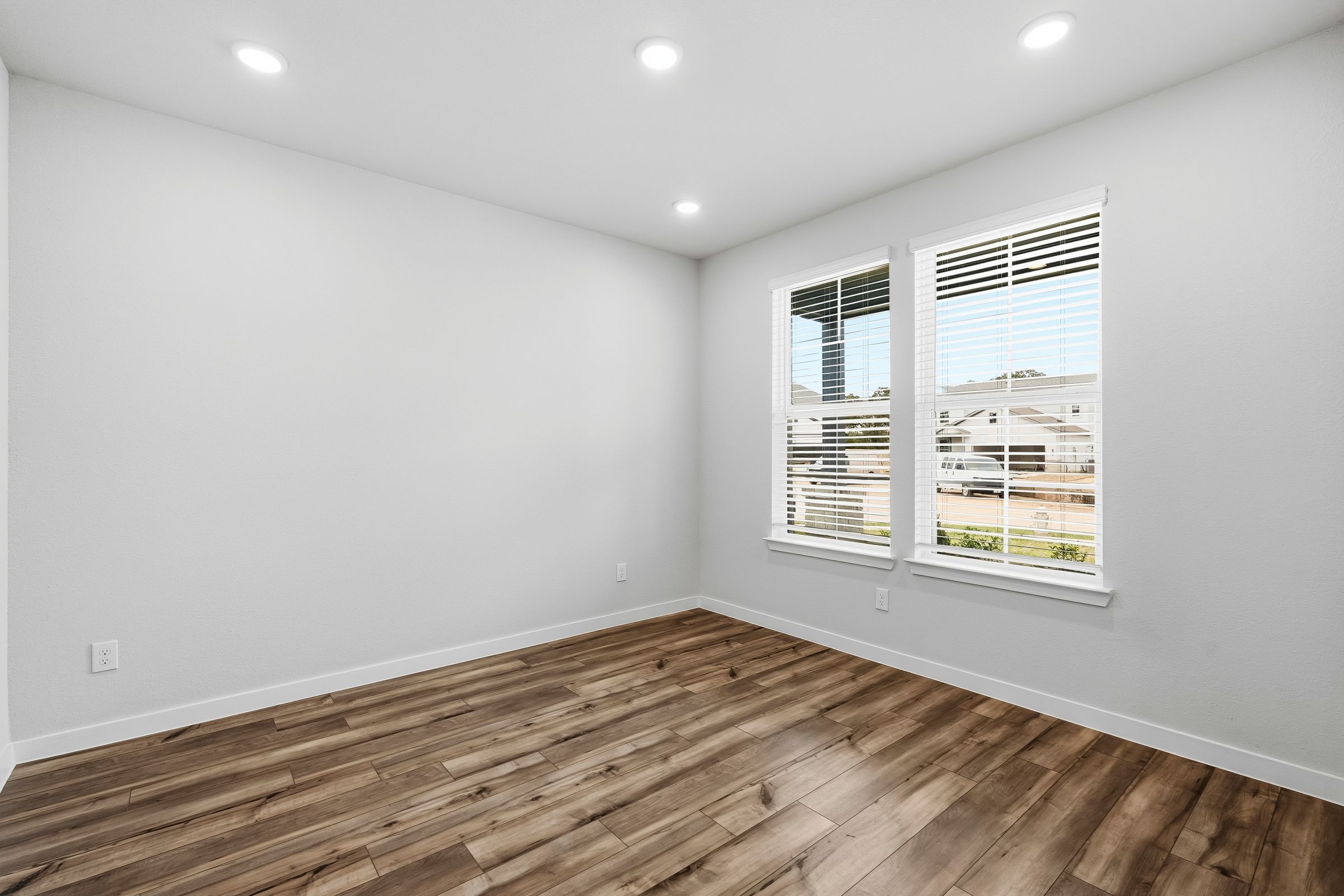 A room with a wood floor and a window with blinds.