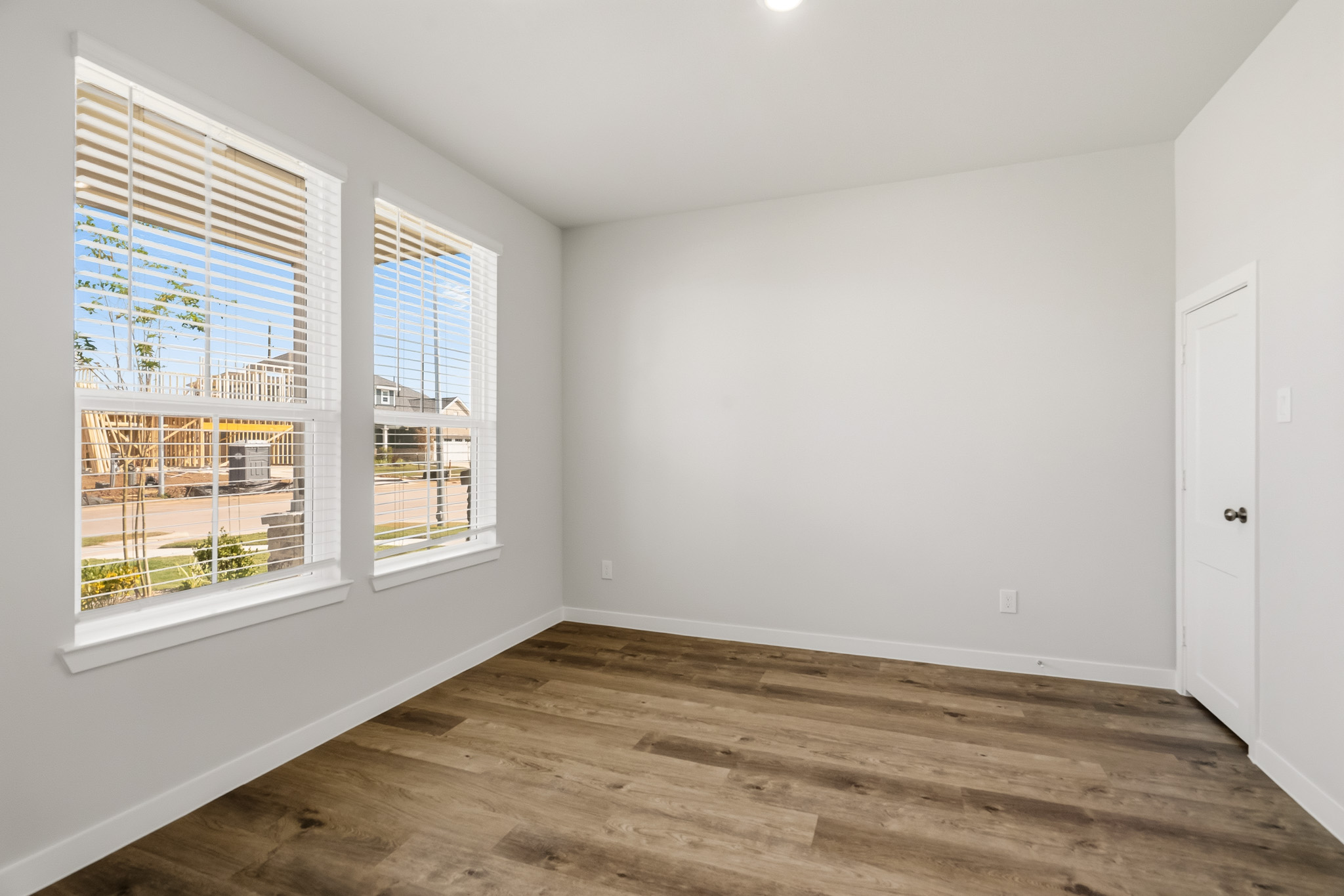 A room with a wood floor and a window with blinds.