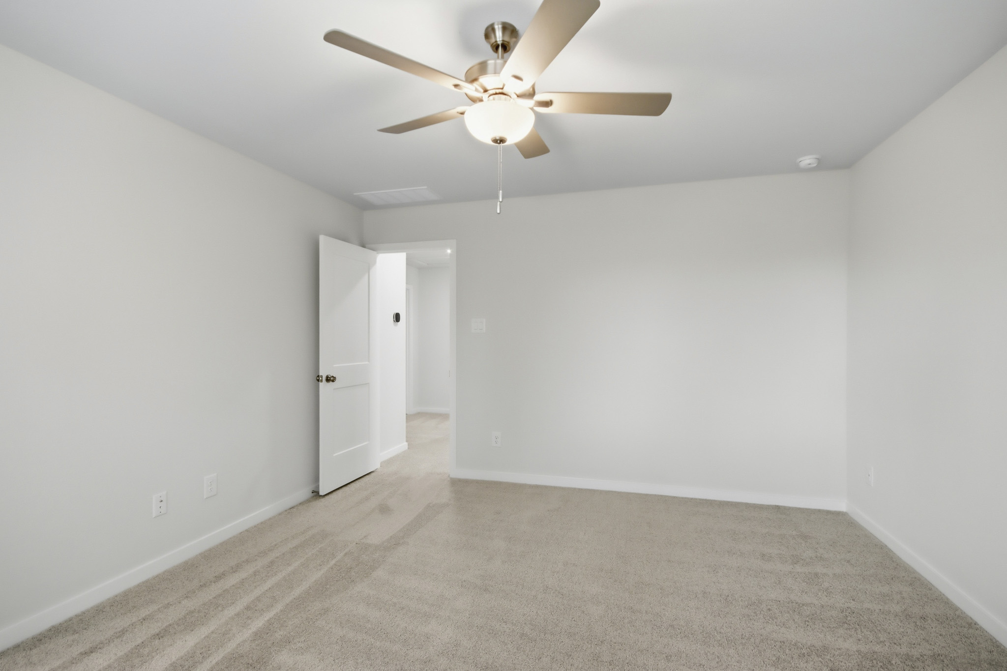 A room with a ceiling fan and white walls.