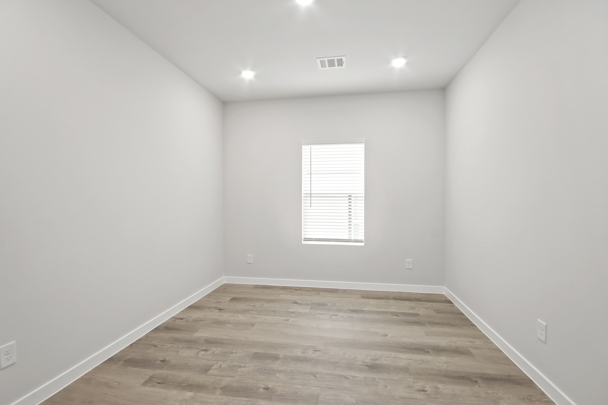 A room with a wood floor and a white wall with a window.