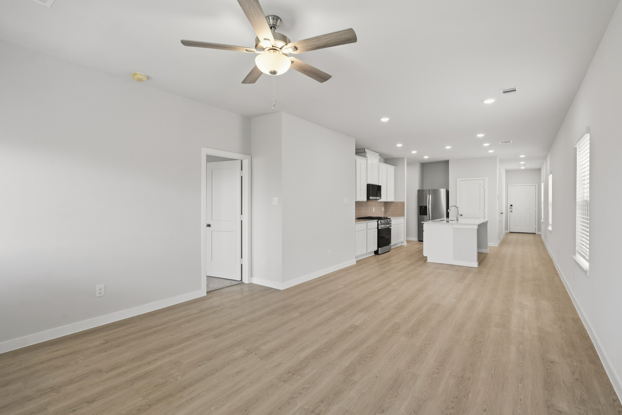 A large empty room with a ceiling fan and white cabinets.