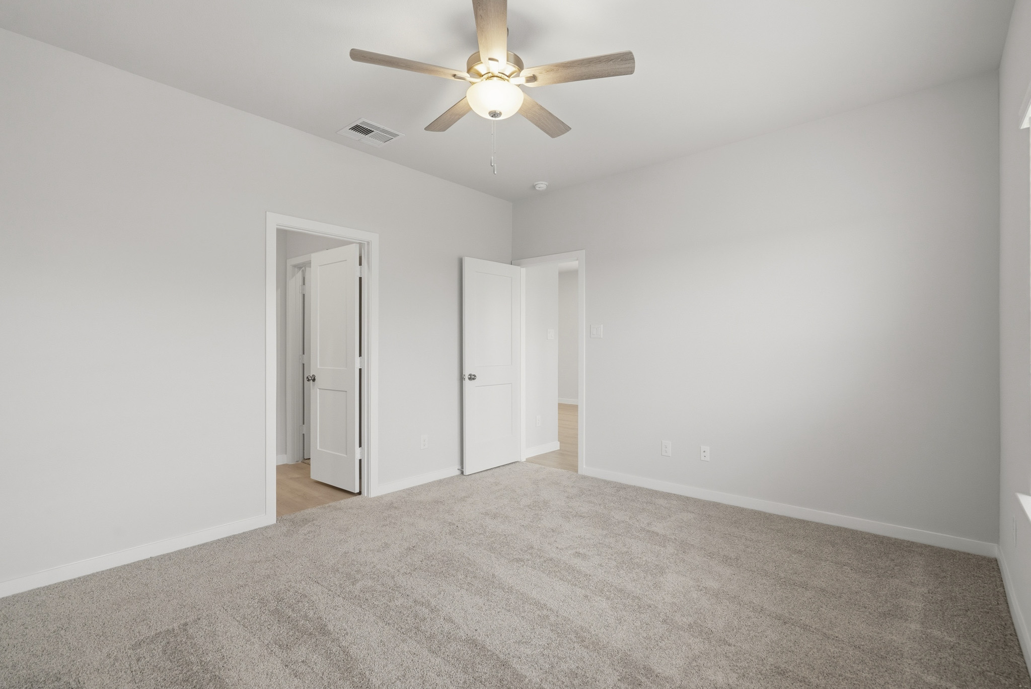 A room with a ceiling fan and a carpet.