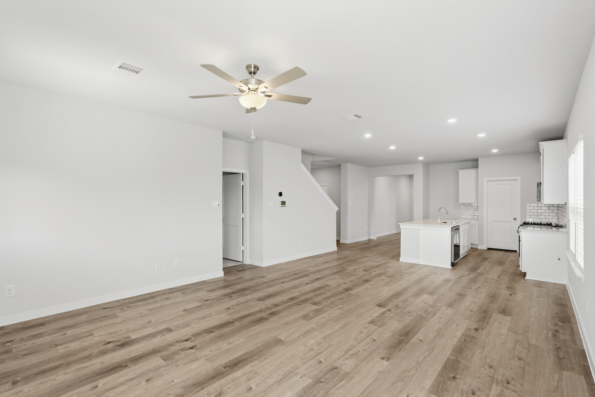 A large empty room with a ceiling fan and white cabinets.