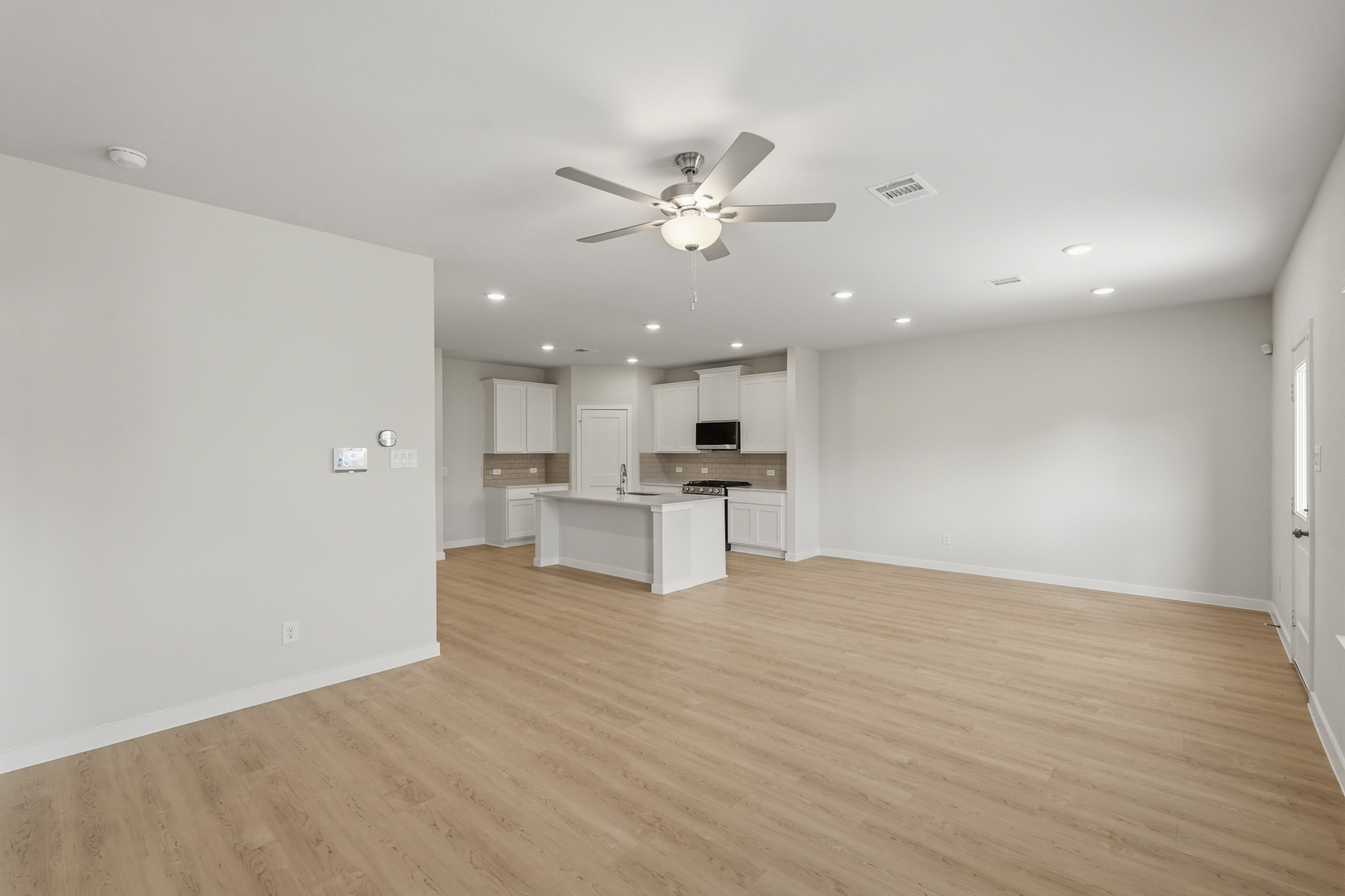 A large empty room with a ceiling fan and a wood floor.