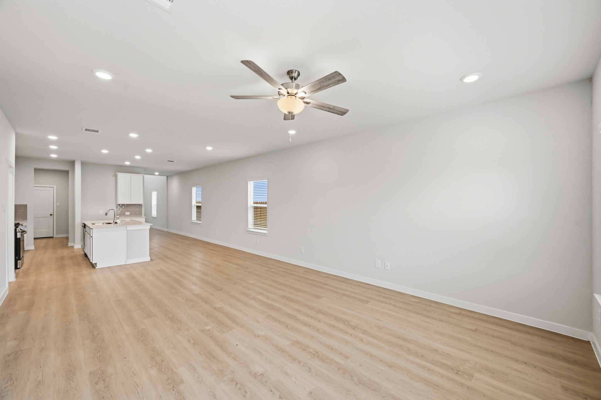 A large empty room with a ceiling fan and a wood floor.