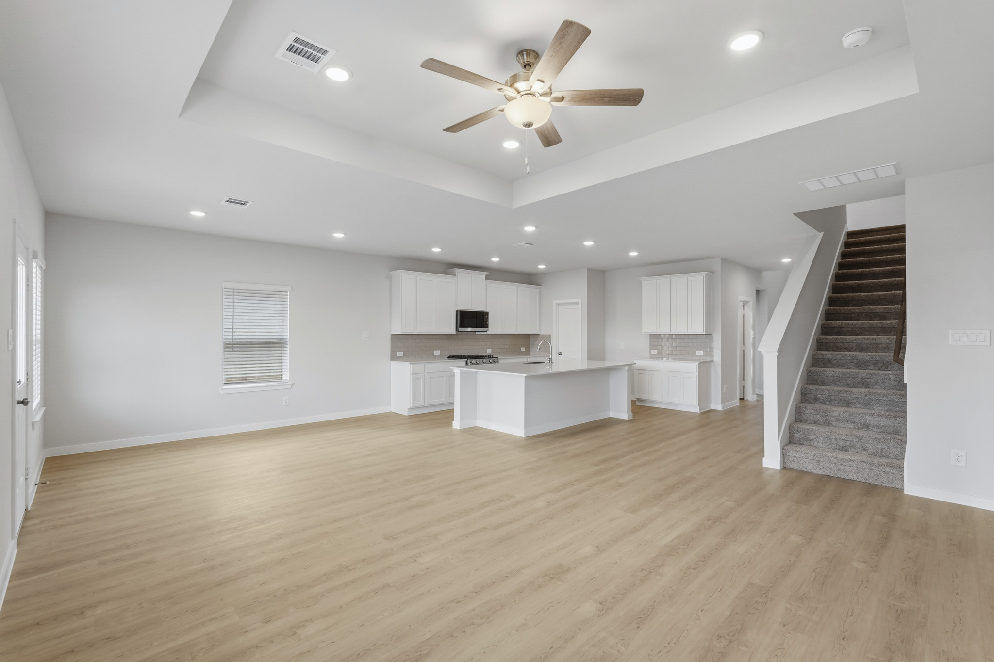 A large empty room with a wood floor and a wood staircase.