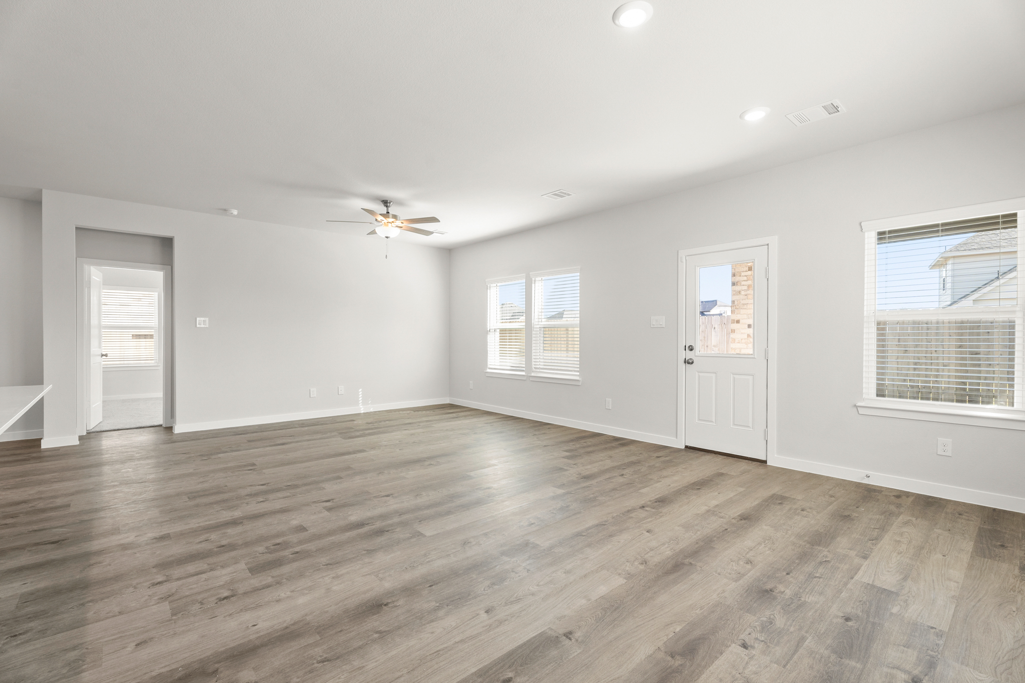 A large empty room with a wood floor and a ceiling fan.