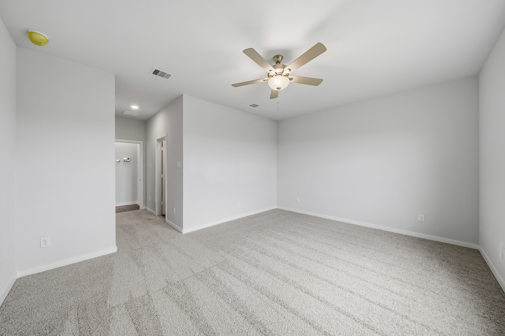 A room with a ceiling fan and a carpet.