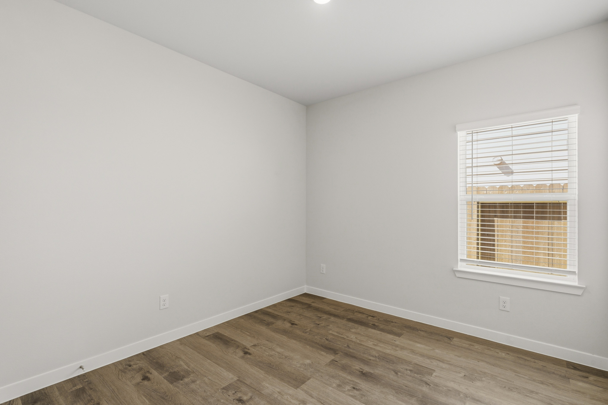 A room with a wood floor and a window with blinds.