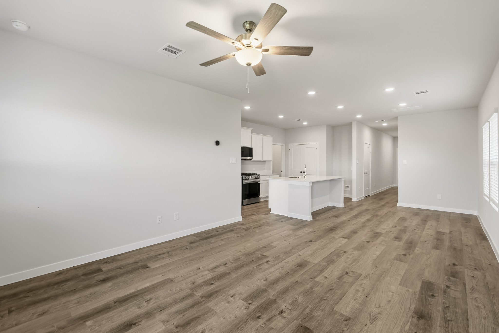 A large empty room with a ceiling fan and a wood floor.