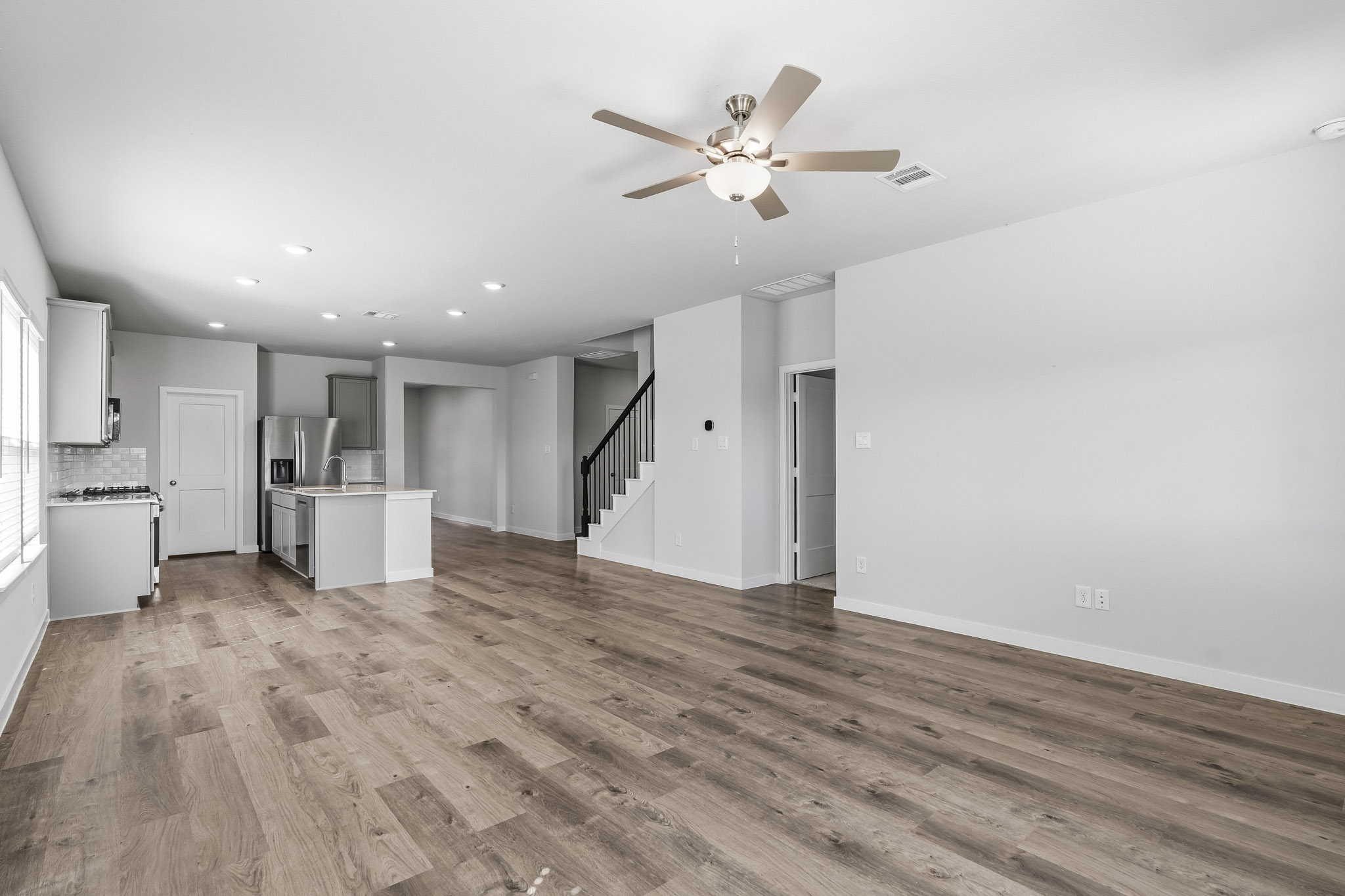A large empty room with a ceiling fan and wood floors.