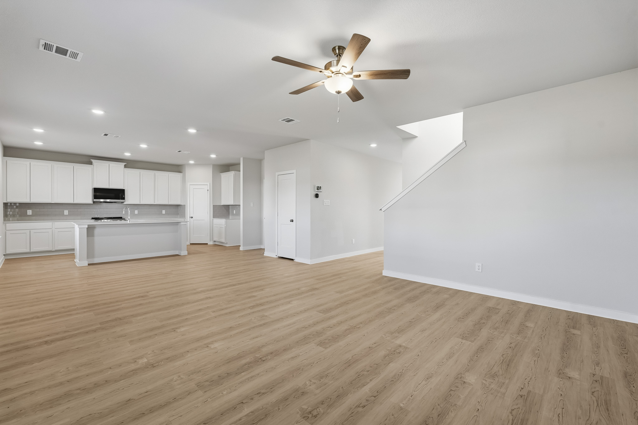 A large empty room with a ceiling fan and white cabinets.