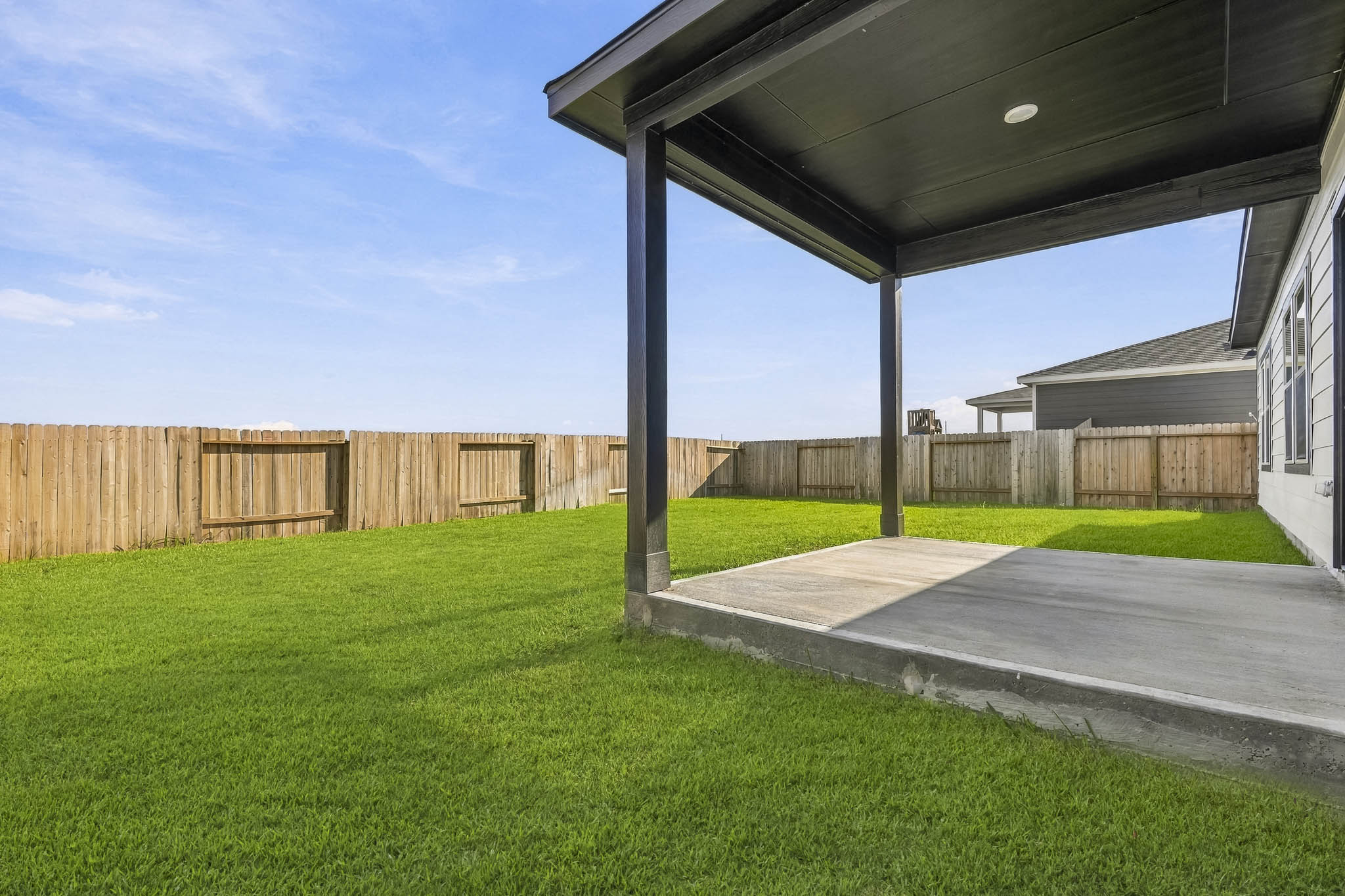 A backyard with a fence and a covered patio.