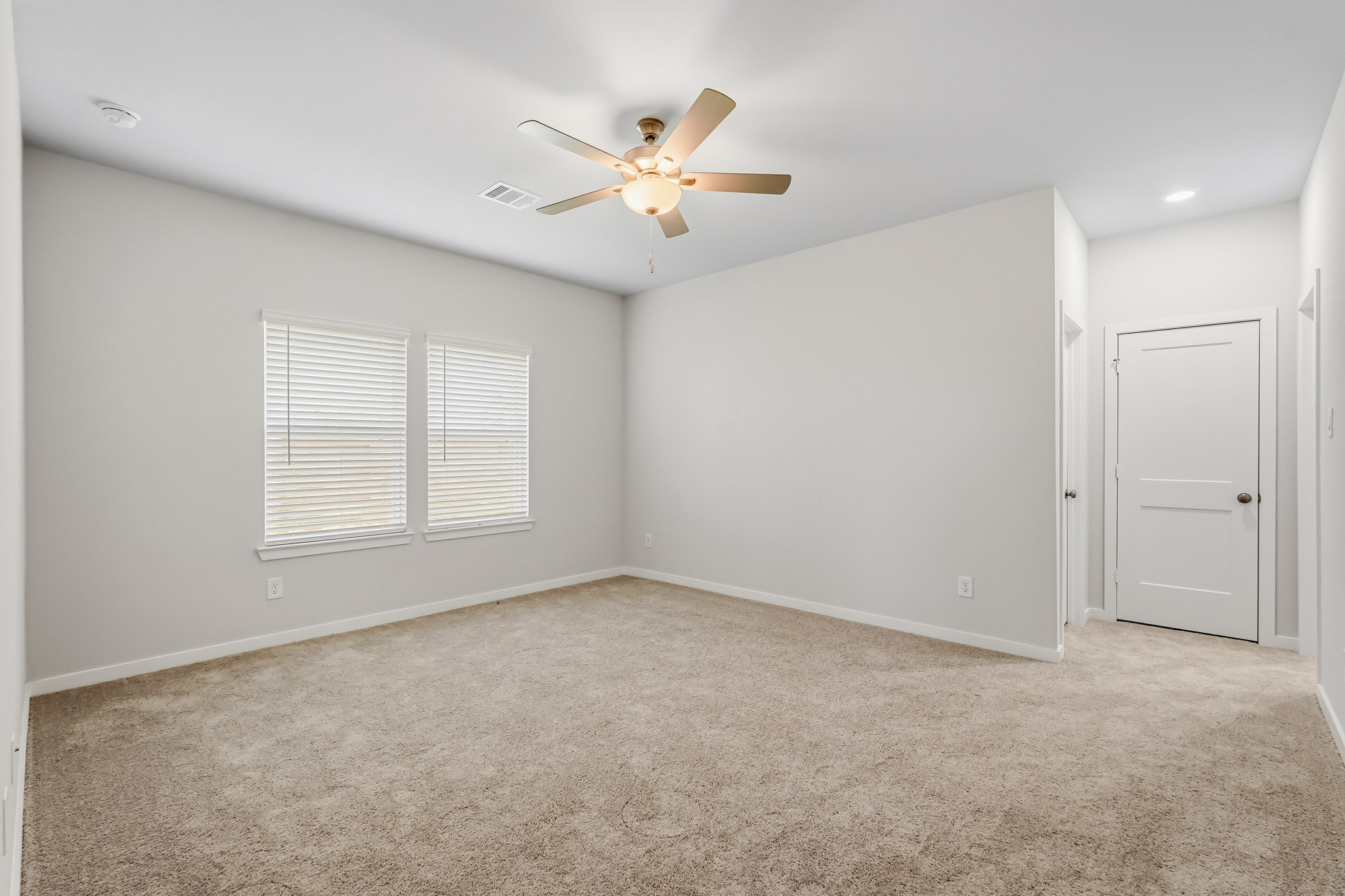 A room with a ceiling fan and a carpet.