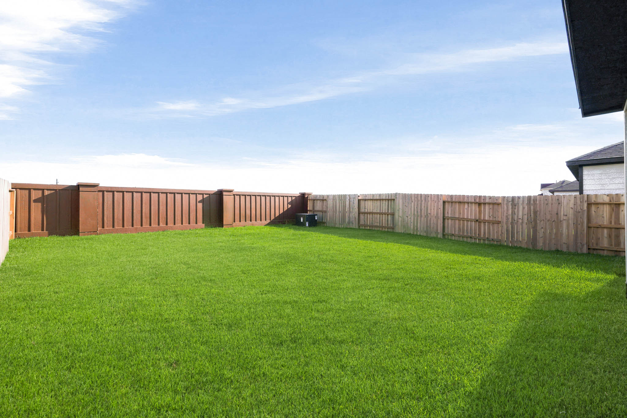A fenced in yard with a wood fence and a building in the background.