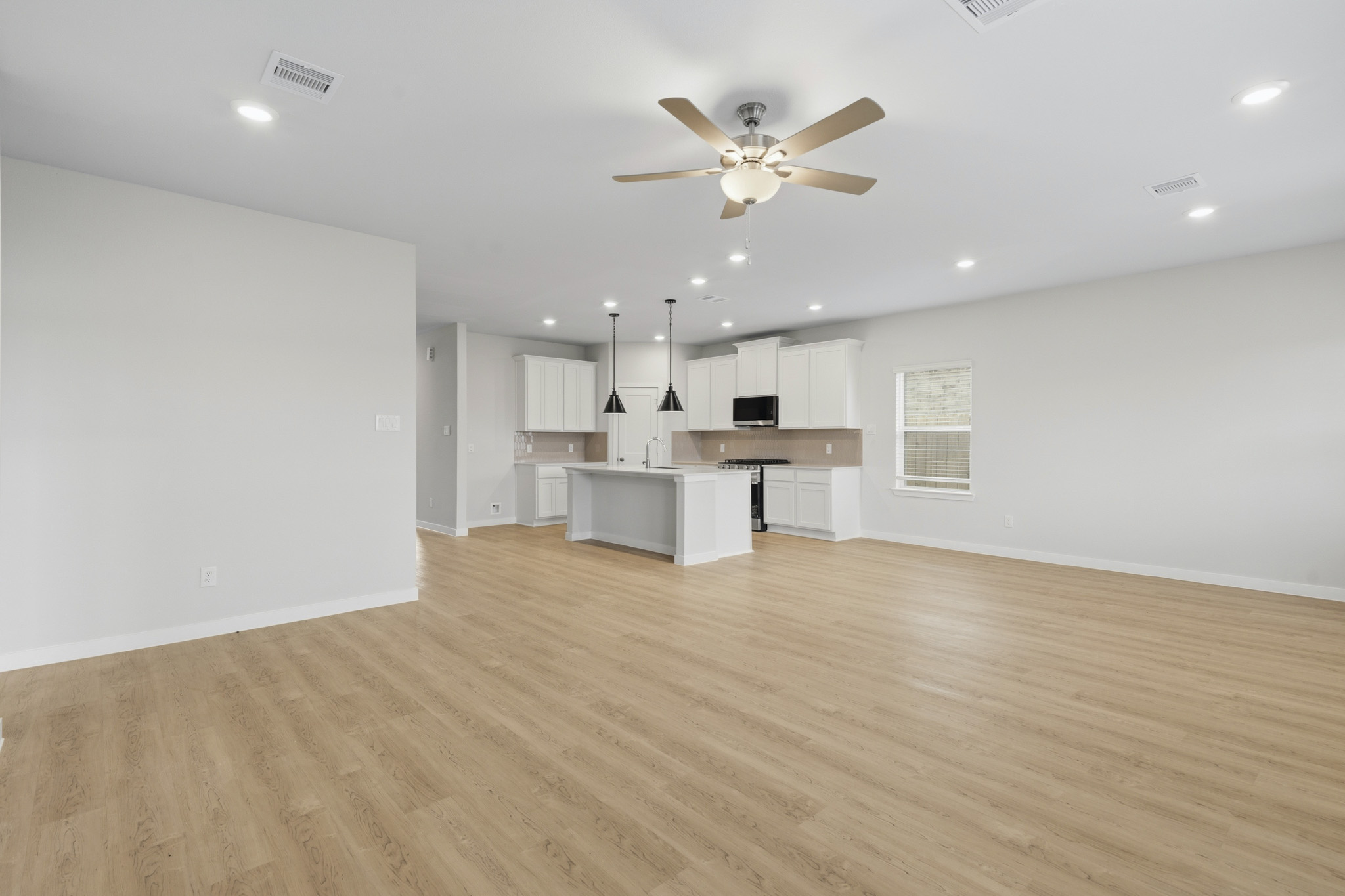 A large empty room with a ceiling fan and a wood floor.