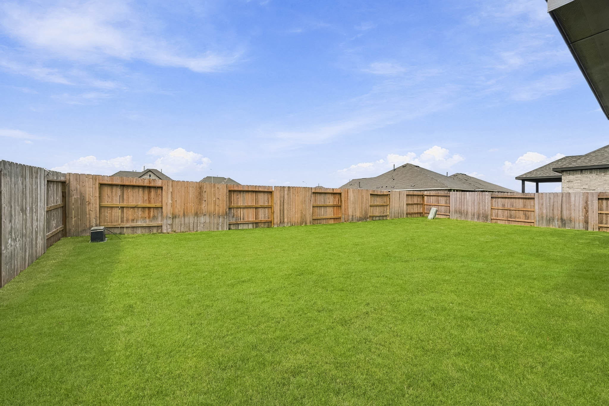 A fenced in yard with a green lawn and a building in the background.