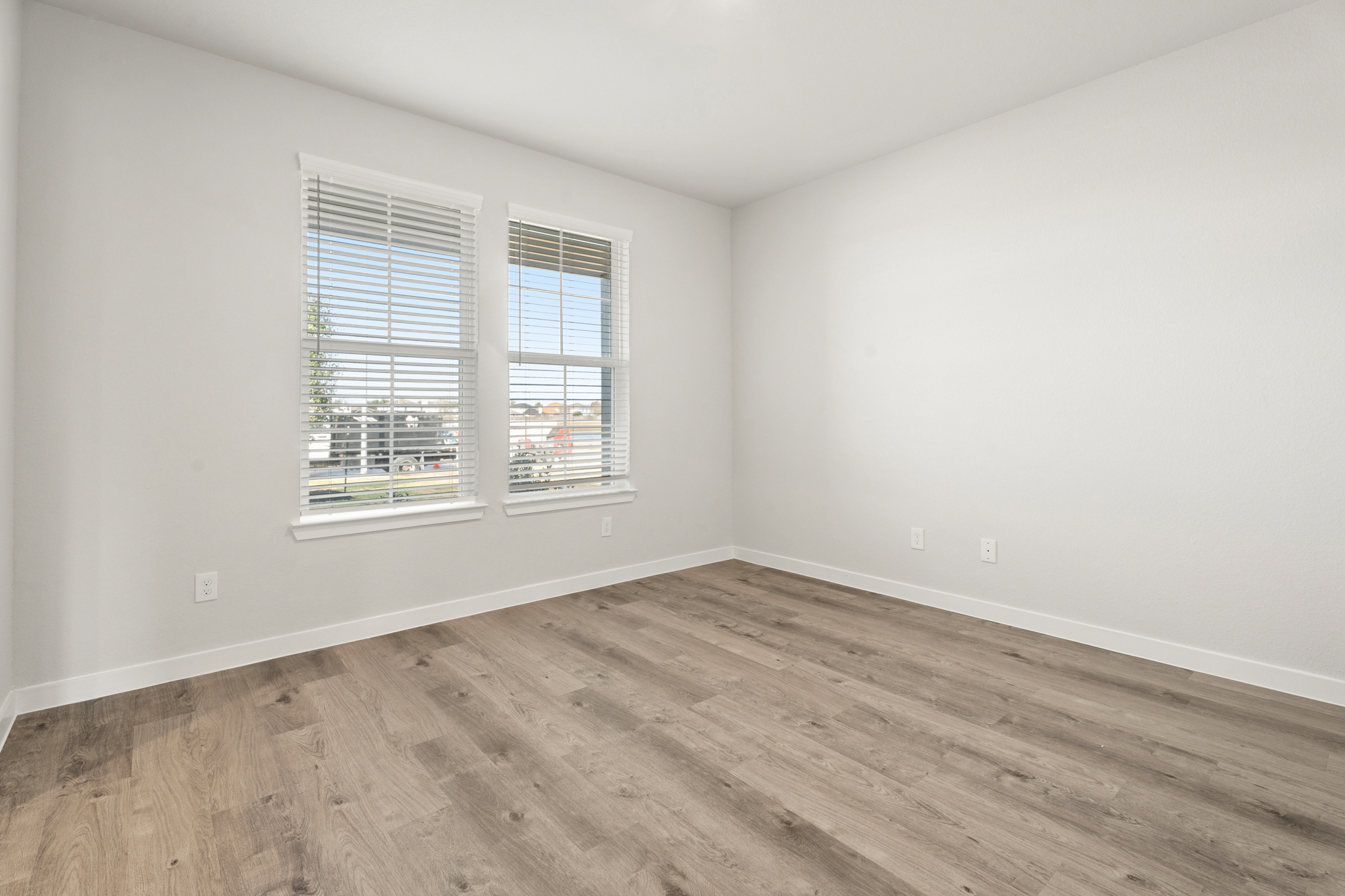 A room with a wood floor and a window with blinds.