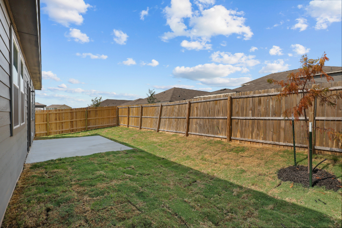 A fenced in yard with a tree and a house in the background.