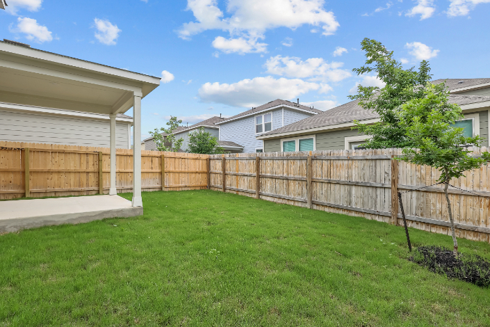 A fenced in yard with a house and trees in the background.