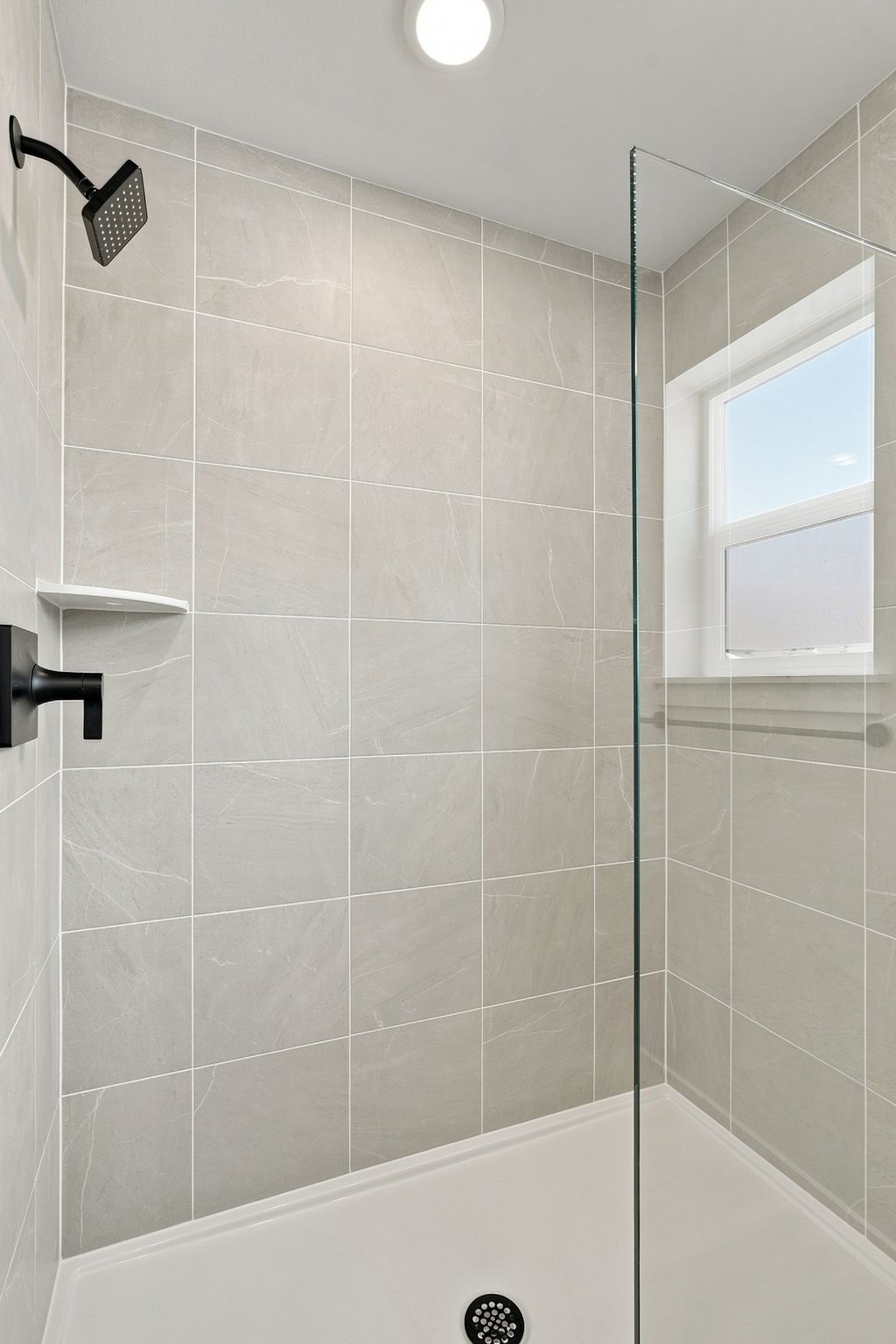 A white tiled shower with a window.