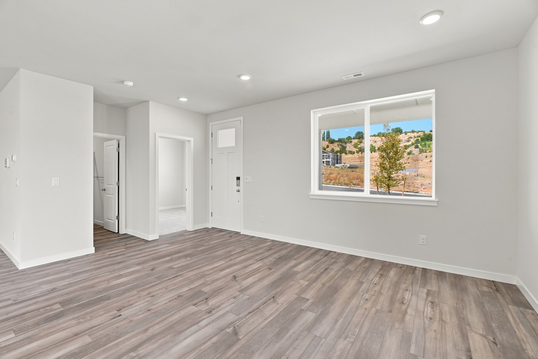 A room with a wood floor and a window with a view of a tree and a building.