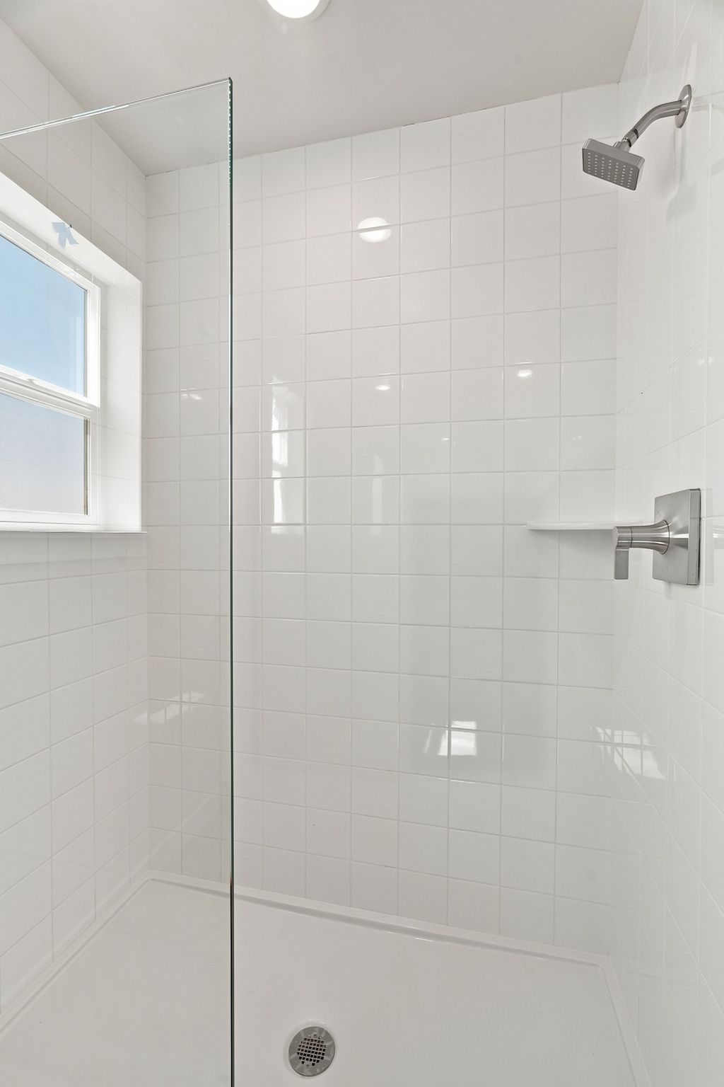 A white tiled shower with a window.