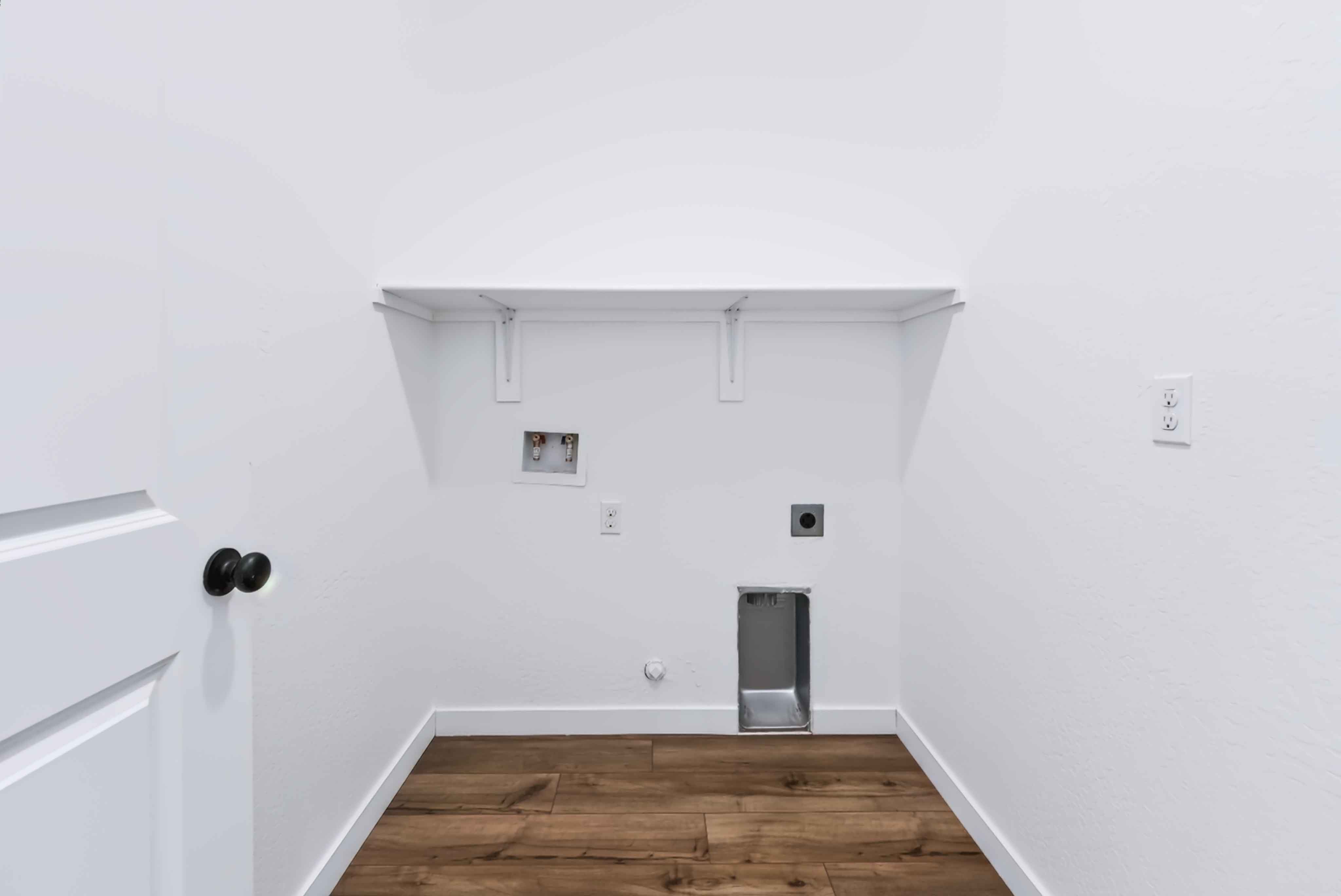 A room with a wood floor and a white wall with a black object.
